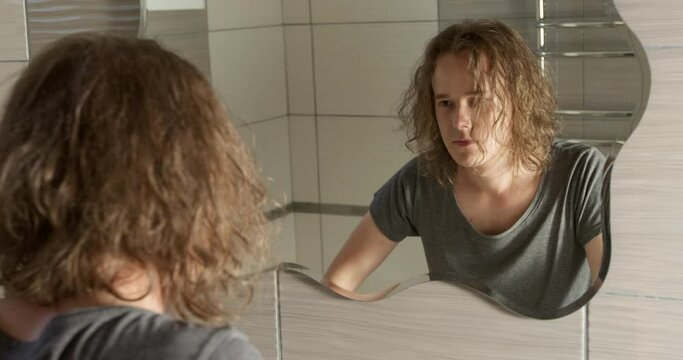 A sad and depressed young man, a teenager, looks in the mirror. The concept of psychological problems and mental health.