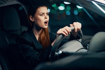 Fototapeta na wymiar a surprised, shocked woman is sitting behind the wheel of a car with her seat belt fastened and her mouth wide open looking at the road. Photo on the topic of safe driving