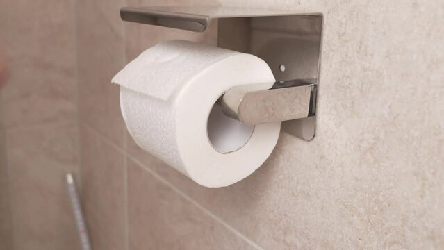 men's hands unwind and tear off a short piece of toilet paper. phone shelf.