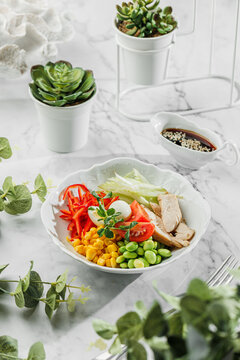 Poke bowl , buddha boul with boled chicken ,boiled eggs, avocado, cherry, corn, cabbage and greens at the white plate on light marble background. Healthy sea food, hard light, restaurant decor