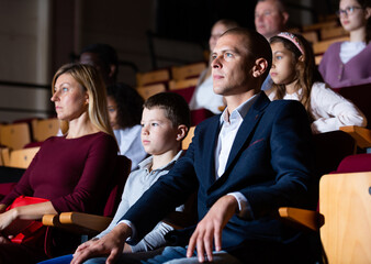 parents with children sitting at premiere in theatrical auditorium - obrazy, fototapety, plakaty