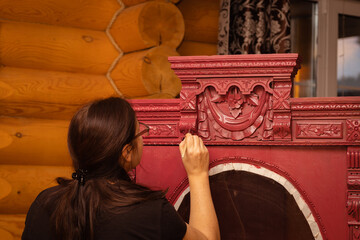 Lady painting splendid carved ornaments on cupboard made of wood in red with brush looking at upper...