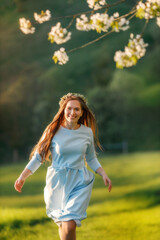 Obraz premium Portrait of beautiful happy woman in blue dress with long hair running forward through green hills during spring. 