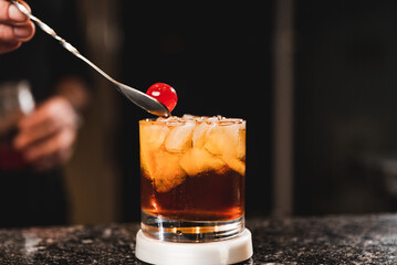 bartender preparing Manhattan drink with cherry and ice
