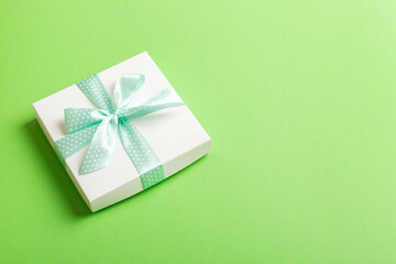 wrapped Christmas or other holiday handmade present in white paper with green ribbon on colored background. Present box, decoration of gift on colored table, top view with copy space
