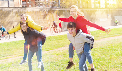 Group of laughing teenagers spending time together on spring day, girls riding piggy-back on boys. Concept of happy adolescence