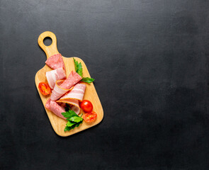 Meat assortment bacon sausage salami slices cherry tomatoes cutting wooden board, black background