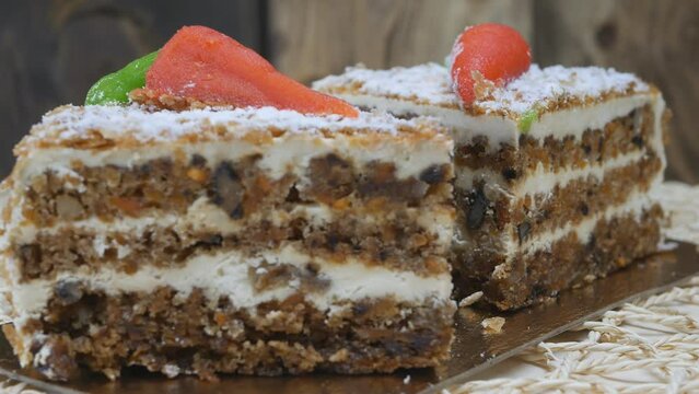 Two pieces of carrot cake rotate slowly. Sponge cake with cream from two layers brown and white. The cake is decorated with orange carrots. Close-up
