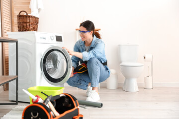 Asian female plumber fixing washing machine in bathroom
