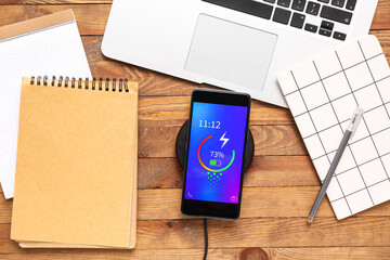 Mobile phone charging with wireless pad, laptop and notebooks on wooden background