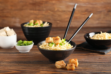Bowls of tasty noodles with chicken on wooden background