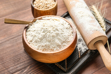 Wheat ear, bowls with flour, rolling pin and board on wooden background, closeup
