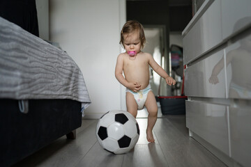 One female toddler caucasian in diapers running in the house with soccer ball Early child...