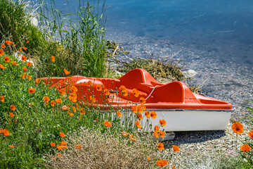 Orange pedal boat on a stone beach at a summer lake. Beautiful idyllic calm landscape at Okanagan lake BC