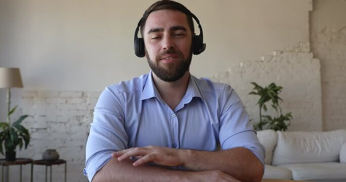Happy confident millennial freelance employee man in headphones with mic waving greeting hand hello at webcam, speaking, talking on video conference call, listening, looking at camera. Head shot