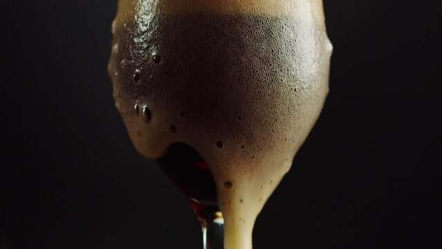 Foamy beer in glass close-up. Cold alcohol stout beer drink in mug. Fresh porter on black background. 