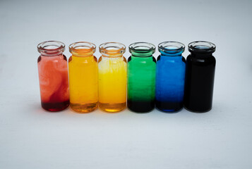 hilera de botellitas con agua coloreada multicolor, arcoiris con fondo blanco 
