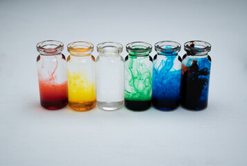 seis botellitas de vidrio con tintas diluidas multicolor y fondo blanco