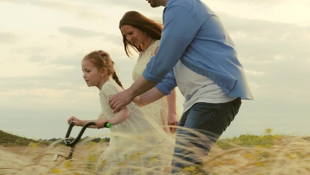 happy parents teach smiling child daughter ride bike. happy family concept. childhood dream ride bike. kid turns handlebars bike. children fast cycling. caring father mother kid daughter park meadow.