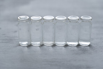 hilera de 6 botellas pequeñas de vidrio sobre fondo con textura claro, llenos de agua, simple y limpio.