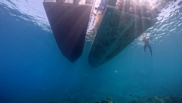 Under Water film of two diving boat hulls. and camera pans up to the surface at ko tao island in Thailand