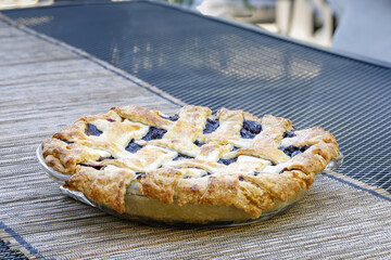 A whole, fresh blueberry pie rest immediately out of the oven and being made ready to serve, enjoy, eat. 