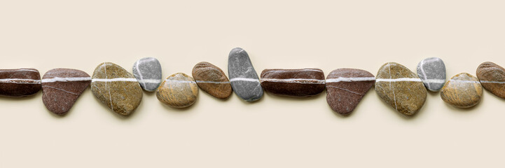 Wide banner with natural colored stones with white stripe. Smooth pebbles in row on beige...