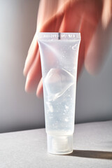 A transparent bottle of cosmetic gel with a blurred hand on the background.