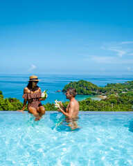 couple European man and an Asian woman in an infinity pool in Thailand looking out over the ocean,...