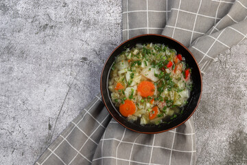 Vegetarian cabbage soup with potatoes, bell peppers, carrots and herbs in bowl on a dark gray background. Top view, flat lay