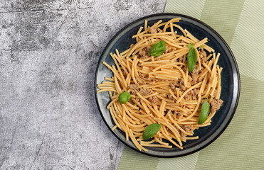 Mince meat pasta with basil leaves on a round plate on a dark gray background. Top view, flat lay