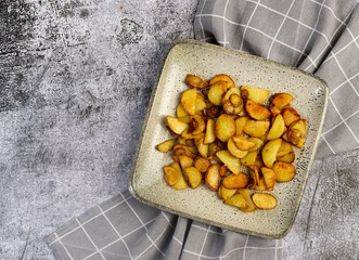 Rustic fried potatoes on a square  plate on a dark background. Top view, flat lay