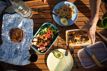 A picnic on a boat consisting of pasta, avocado and fruit salad with bread.