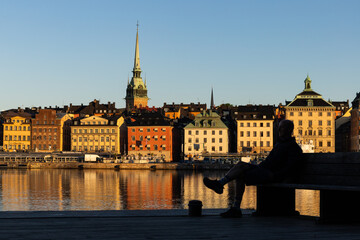 Fototapeta premium Stockholm, Sweden A man sits on a bench on Skeppsholmen with a view over water and Gamla Stan, or Old Town.