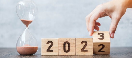 hand flip block 2022 to 2023 text with hourglass on table. Resolution, time, plan, goal,...