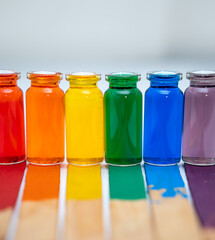 hilera de botellitas con agua coloreada multicolor, arcoiris con fondo blanco y palitos de madera en la base