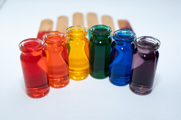 hilera de botellitas con agua coloreada multicolor, arcoiris con fondo blanco y palitos de madera en la base