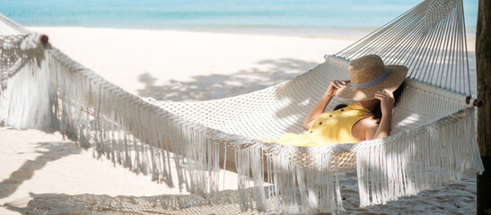 Happy Woman Traveler is relaxing in a hammock on the paradise beach. Female tourist in yellow dress...