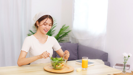 Lifestyle in living room concept, Young Asian woman mixing vegetable salad in bowl for breakfast
