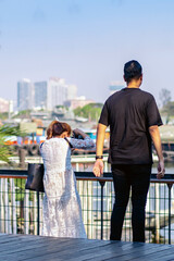 Back view portrait of attractive Asian woman photographer or traveller using a professional mirrorless camera take photo at riverside on sunny day during weekend trip. Attractions and travel concept.