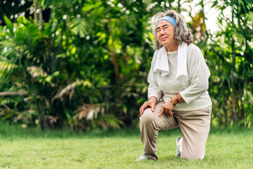 Sick unhappy senior adult elderly asian woman touching her muscle injury leg suffering from muscles knee pain ache in park at home.physical injury and  healthcare problem