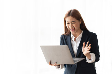 Portrait of an excited young asian business woman holding laptop computer and celebrating success isolated over white background, copy space.