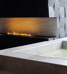 Luxurious bath next to artificial fire in a modern fireplace.