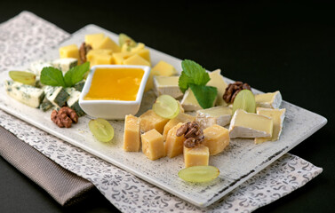 Cheese plate with honey, grapes and nuts on black table, flat lay