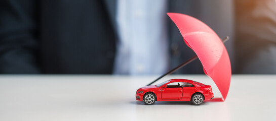 Businessman hand holding umbrella and cover  red car toy on table. Car insurance, warranty, repair,...