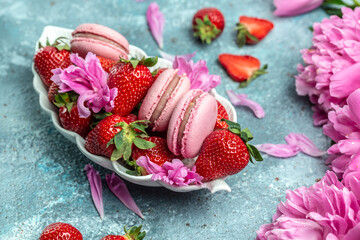 Pink peony rose flower and macaroni cookies and sweet strawberry on blue background. Small French cakes Macarons with fruit. top view