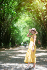 Asian Woman in yellow dress and hat Traveling at green Bamboo Tunnel, Happy traveler walking...