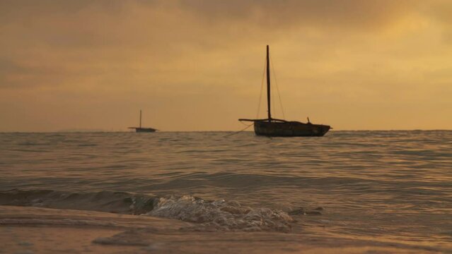 Silhouettes Of Empty Fishing Boats During Warm Yellow And Orange Golden Hour Sunset With Small Waves Breaking On Beach Shore in Vilanculos Bazaruto Archipelago, Mozambique, Africa.