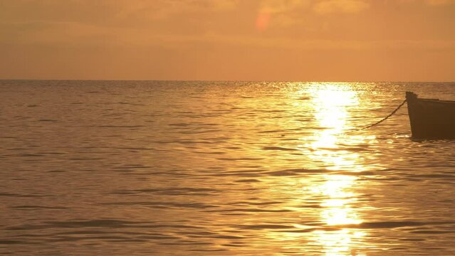 Warm Golden Sunset Light Reflection Off Of Calm Ocean Surface Waves And Ripples With Silhouette Of Anchored Fishing Boat In Vilanculos Bazaruto Archipelago, Mozambique, Africa.