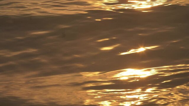 Golden Hour Sunset Light Glowing On Calm Ocean Surface Waves and Ripples. Close Up Shot. 